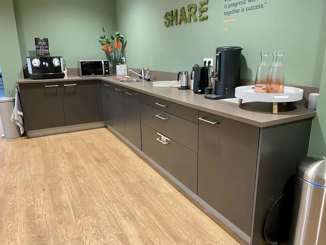 Bedrijfskoffiecorner bij FlexOffiZ Bodegraven met koffieapparaten, waterkokers, een magnetron en glazen flessen op een aanrecht.