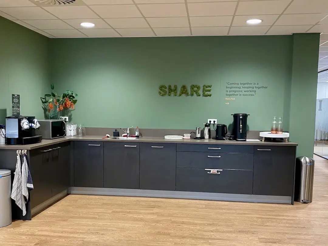 Kleine bedrijfskeuken in FlexOffiZ Bodegraven met koffieapparaten, magnetron en decoratieve wandtekst "SHARE".