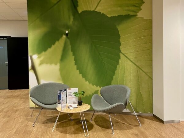 Wachtruimte bij FlexOffiZ Bodegraven met twee moderne stoelen, een ronde tafel en een muur met grote groene bladeren.