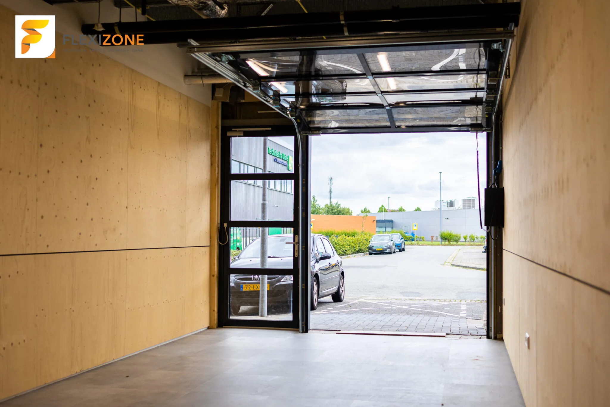 Binnenruimte van Flexizone met open garagedeur die uitzicht biedt op de parkeerplaats en buitenomgeving.