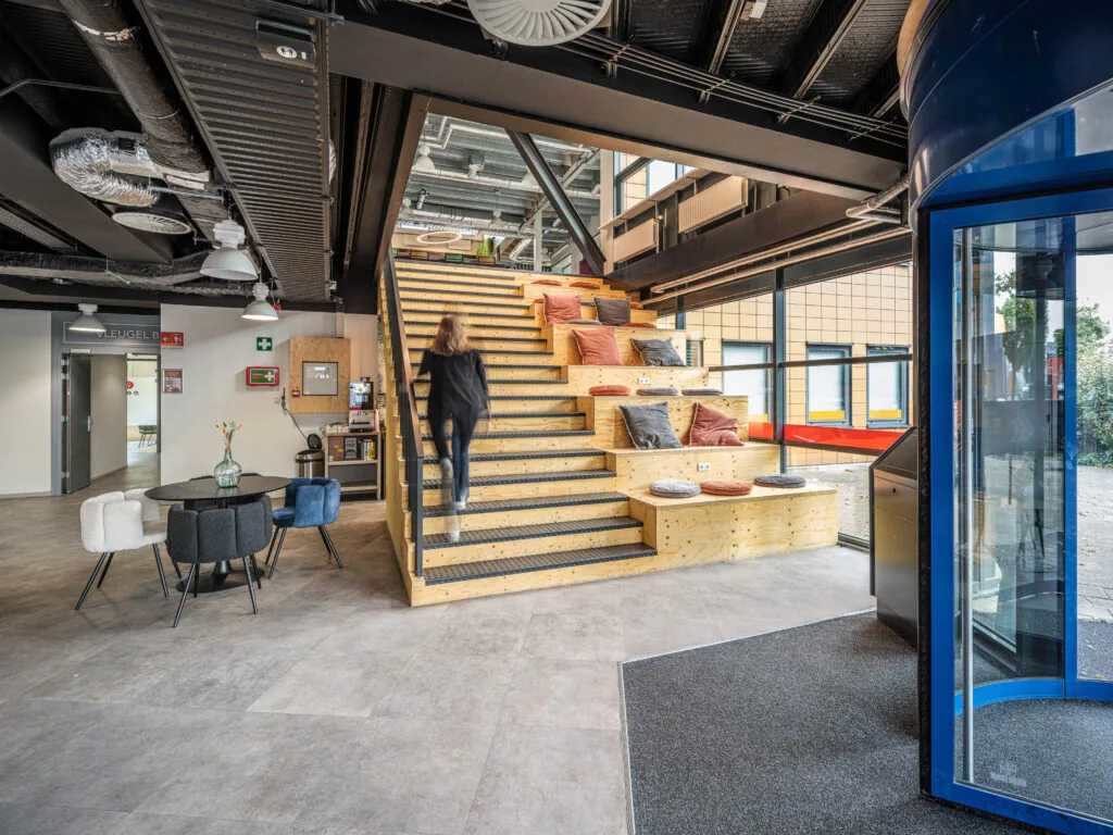 Moderne kantoorruimte van Flexizone met houten tribunetrap, kleurrijke kussens en een open, industriële inrichting.