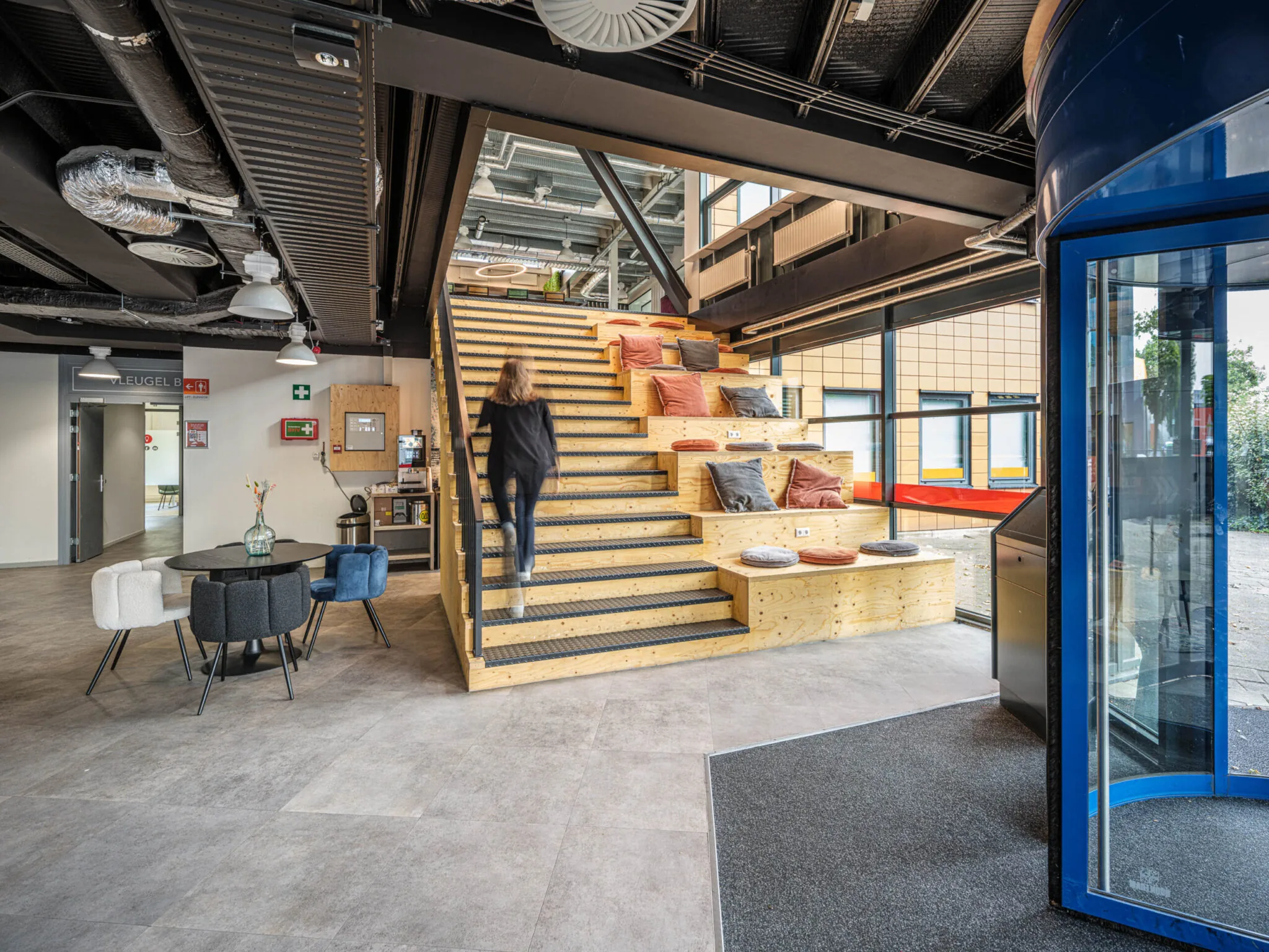 Moderne kantoorruimte van Flexizone met houten tribunetrap, kleurrijke kussens en een open, industriële inrichting.