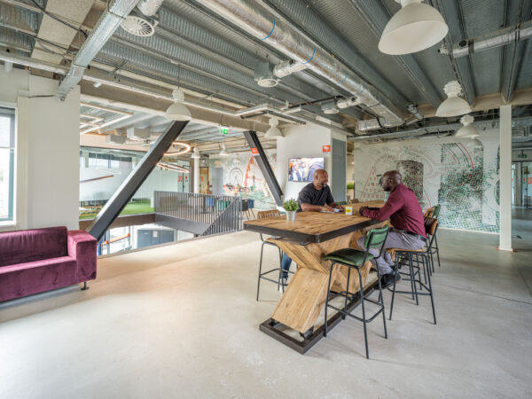 Twee mannen zitten aan een hoge houten tafel in een moderne, industriële kantoorruimte van Flexizone.