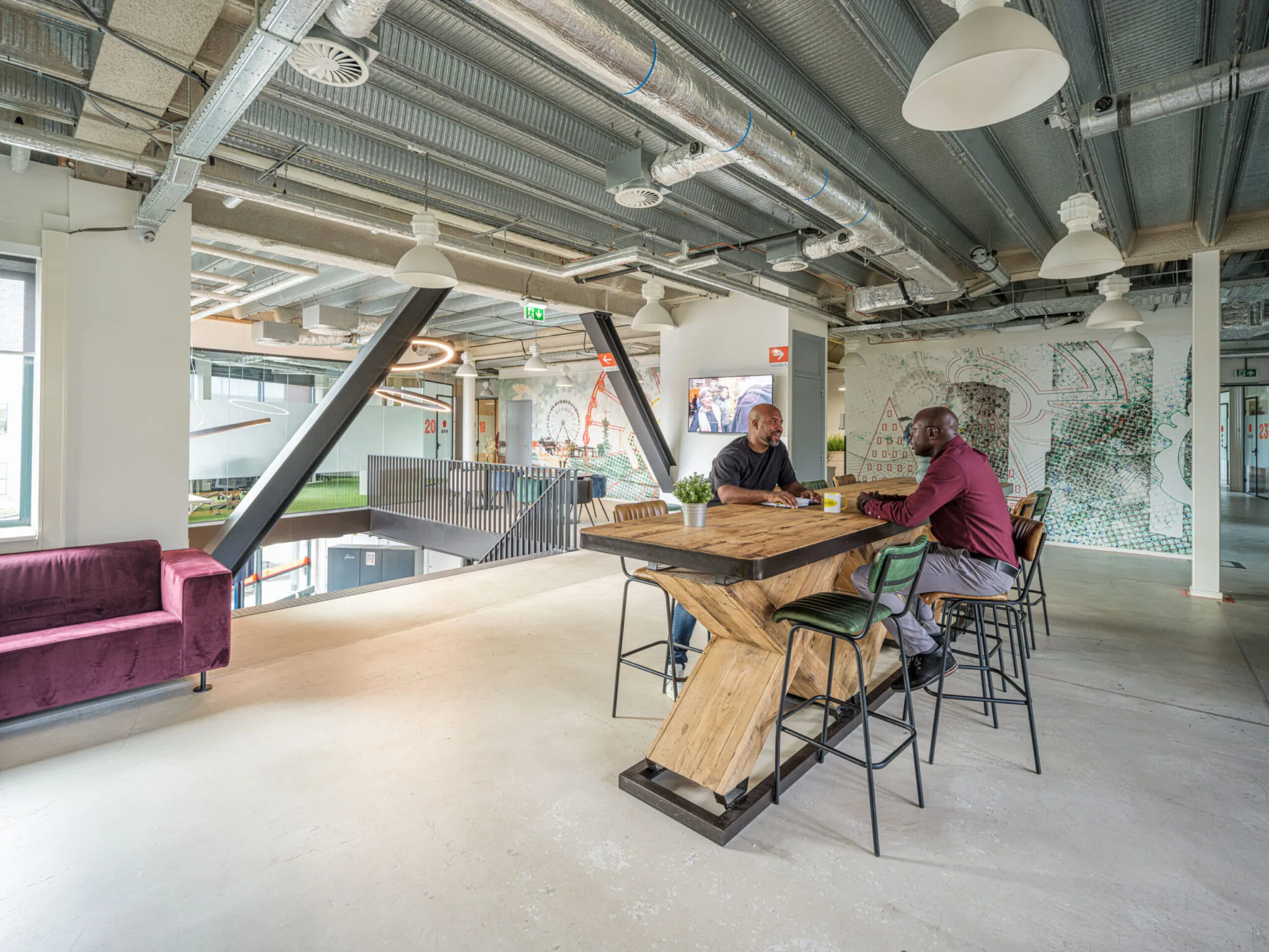 Twee mannen zitten aan een hoge houten tafel in een moderne, industriële kantoorruimte van Flexizone.