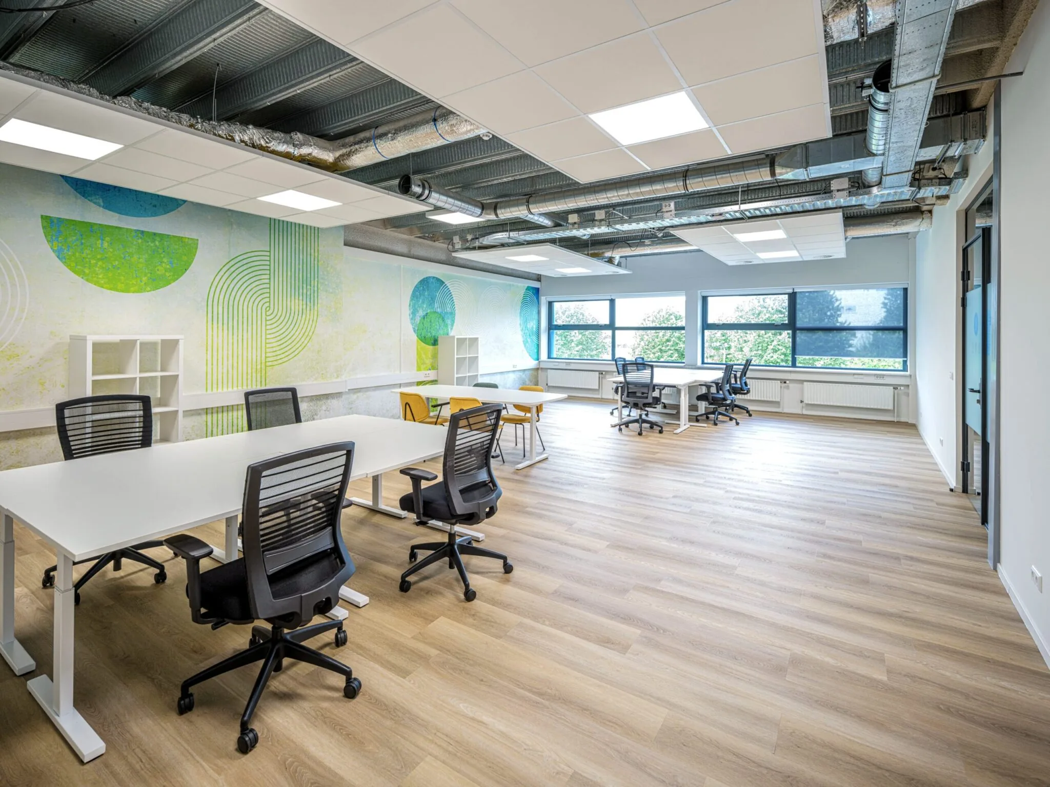 Ruime en moderne Flexizone-kantoorruimte met bureaus, bureaustoelen en kleurrijke muurdecoratie.