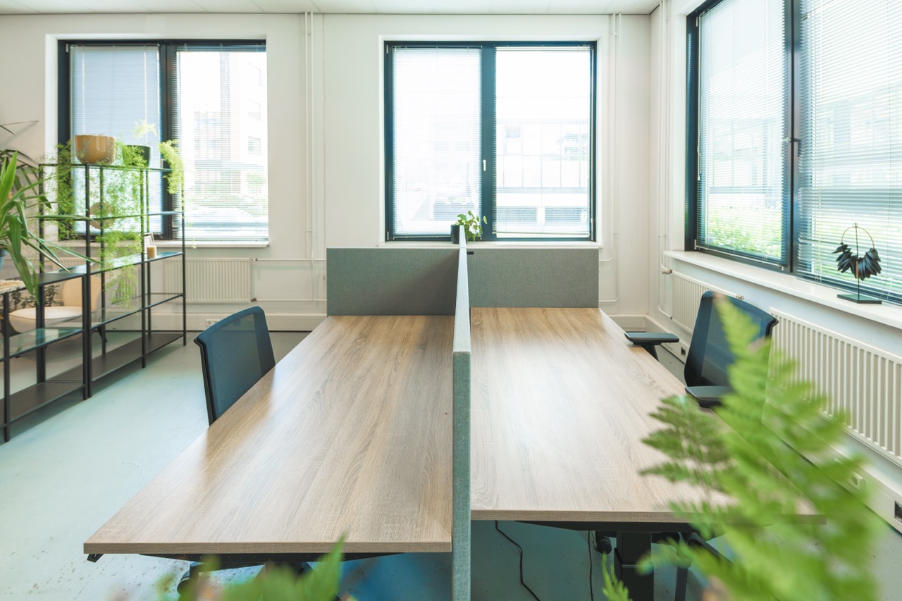 Moderne en lichte flexwerkplek met vier houten bureaus, bureaustoelen en veel groen in een open kantoorruimte.
