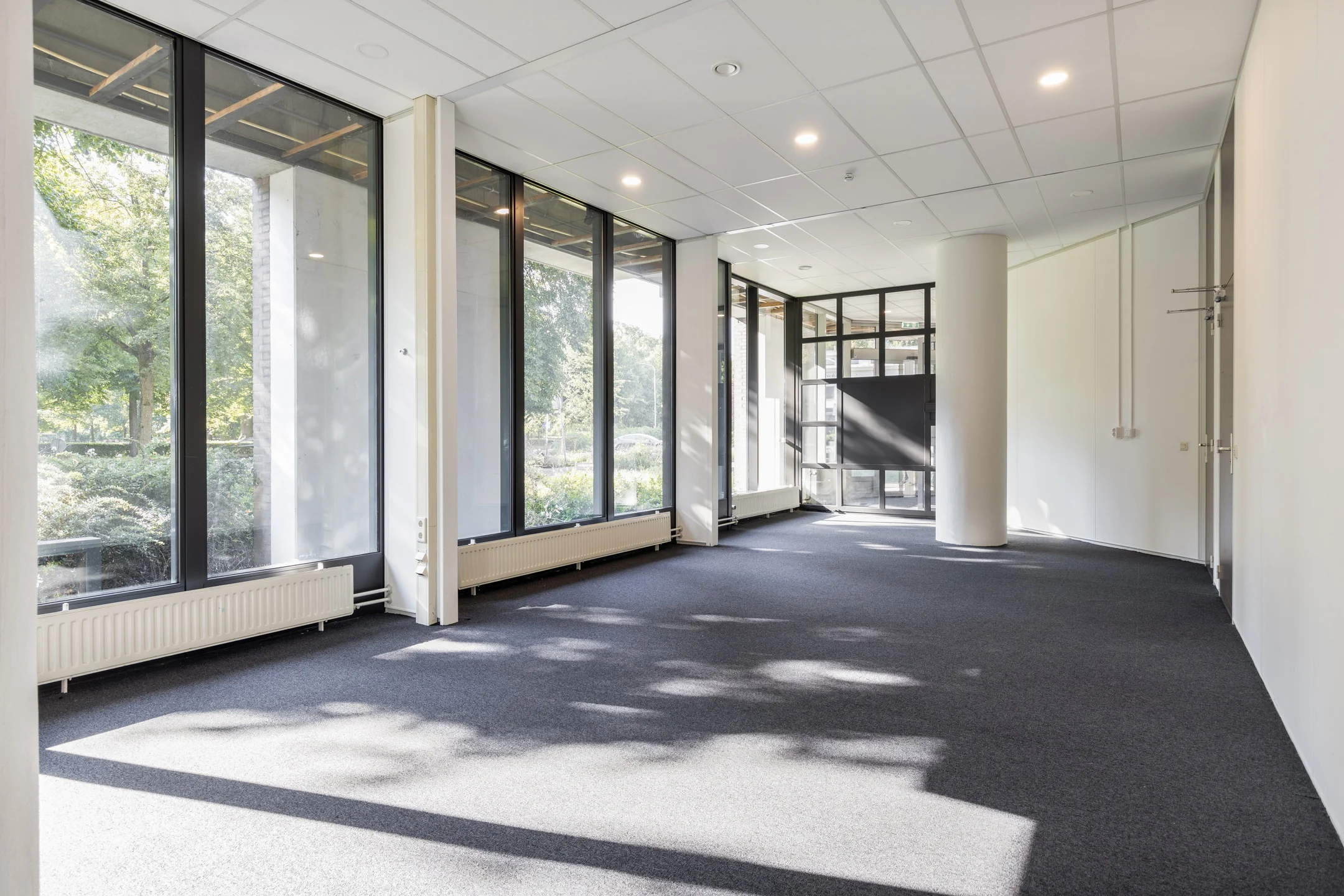 Lichte kantoorruimte aan de Fonteinlaan 5 in Haarlem met grote ramen en donker tapijt.