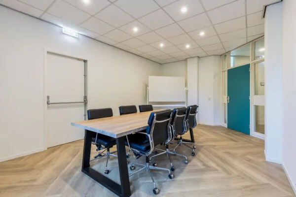 Vergaderruimte in Fonteinlaan 5 in Haarlem met houten tafel, acht zwarte stoelen en een whiteboard.