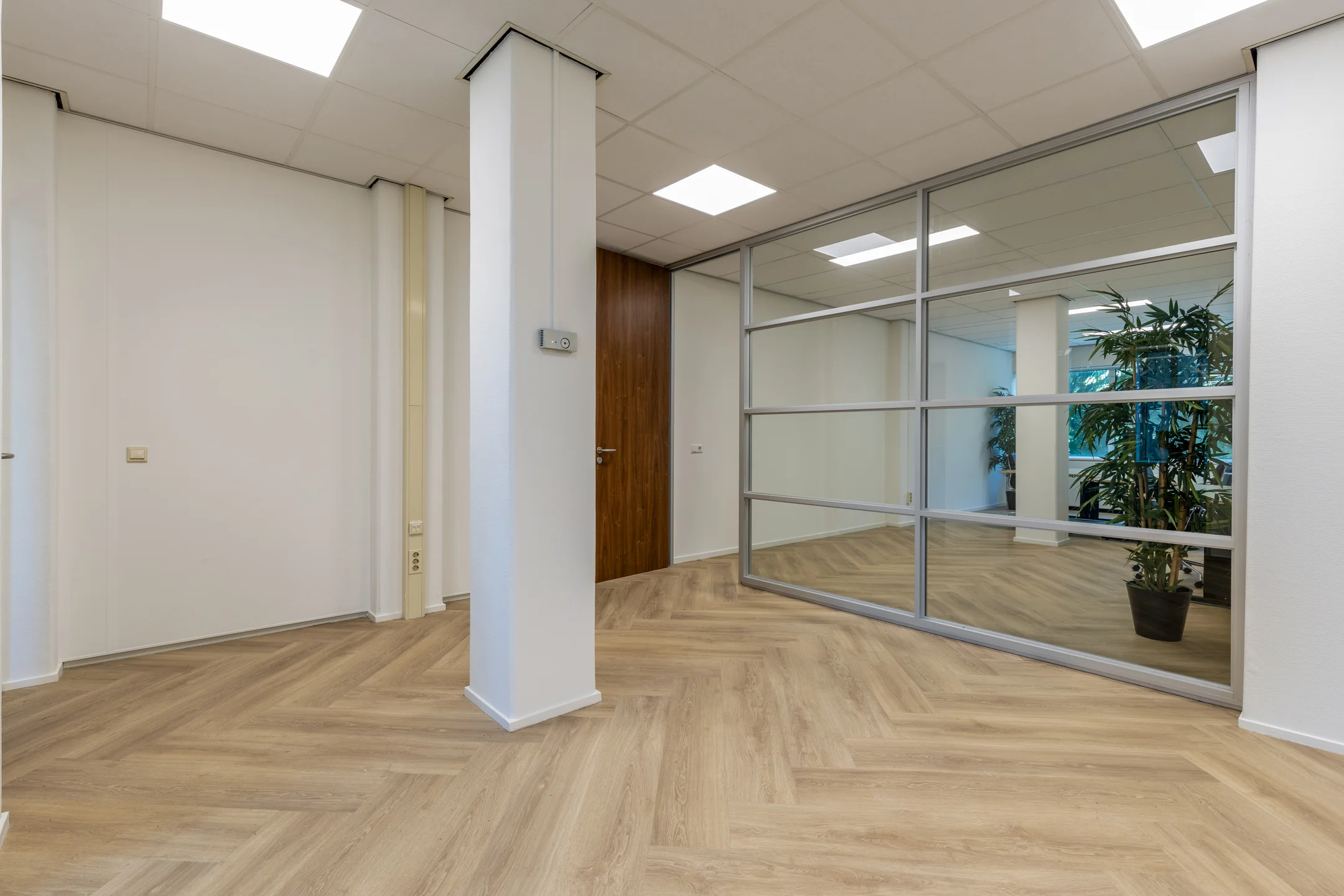 Modern kantoorinterieur aan de Fonteinlaan 5 in Haarlem met houten visgraatvloer, glazen wand en houten deur.