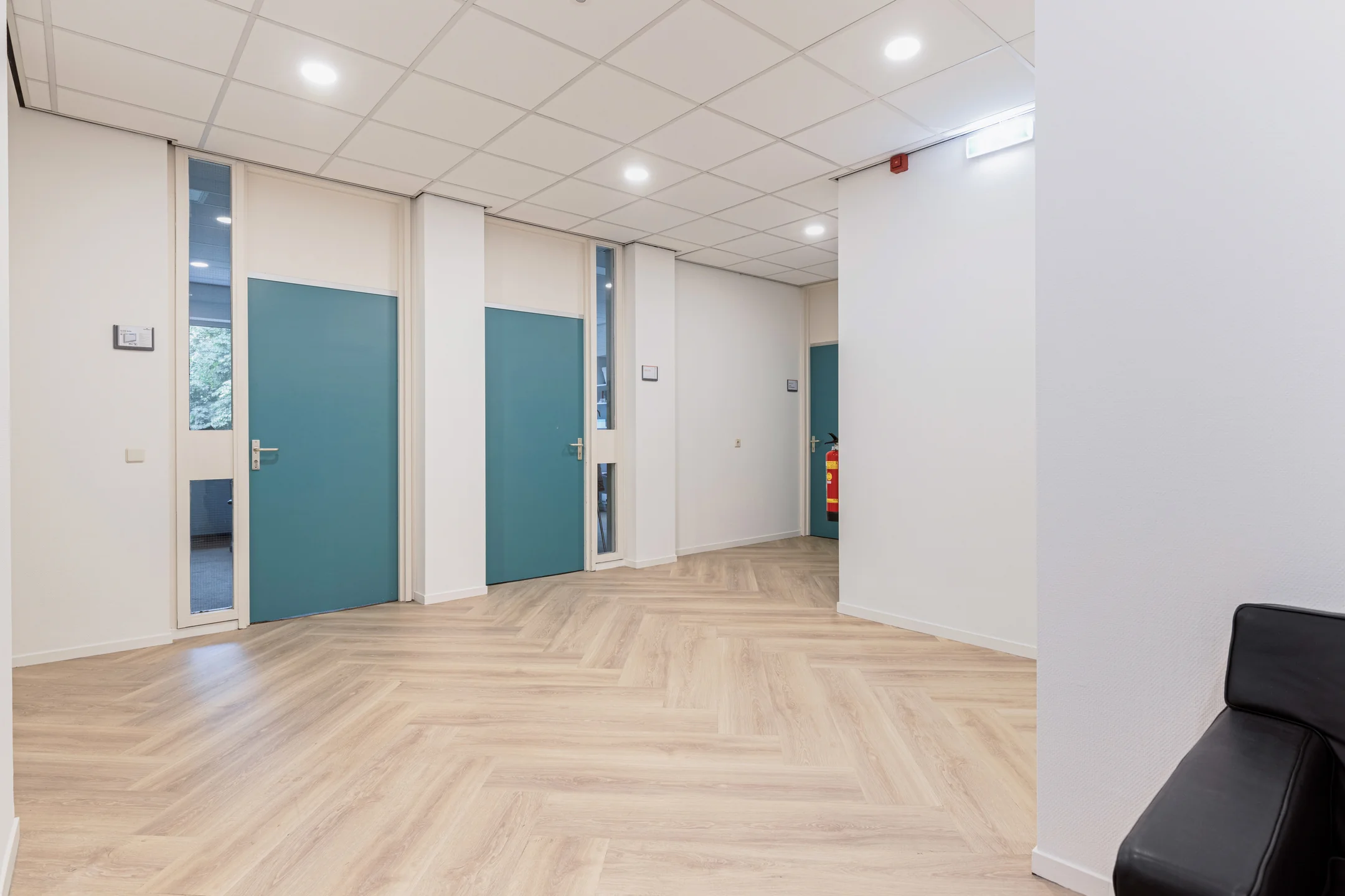 Moderne, lichte gang met houten visgraatvloer, turquoise deuren en witte muren in kantoorgebouw aan de Fonteinlaan 5 in Haarlem.