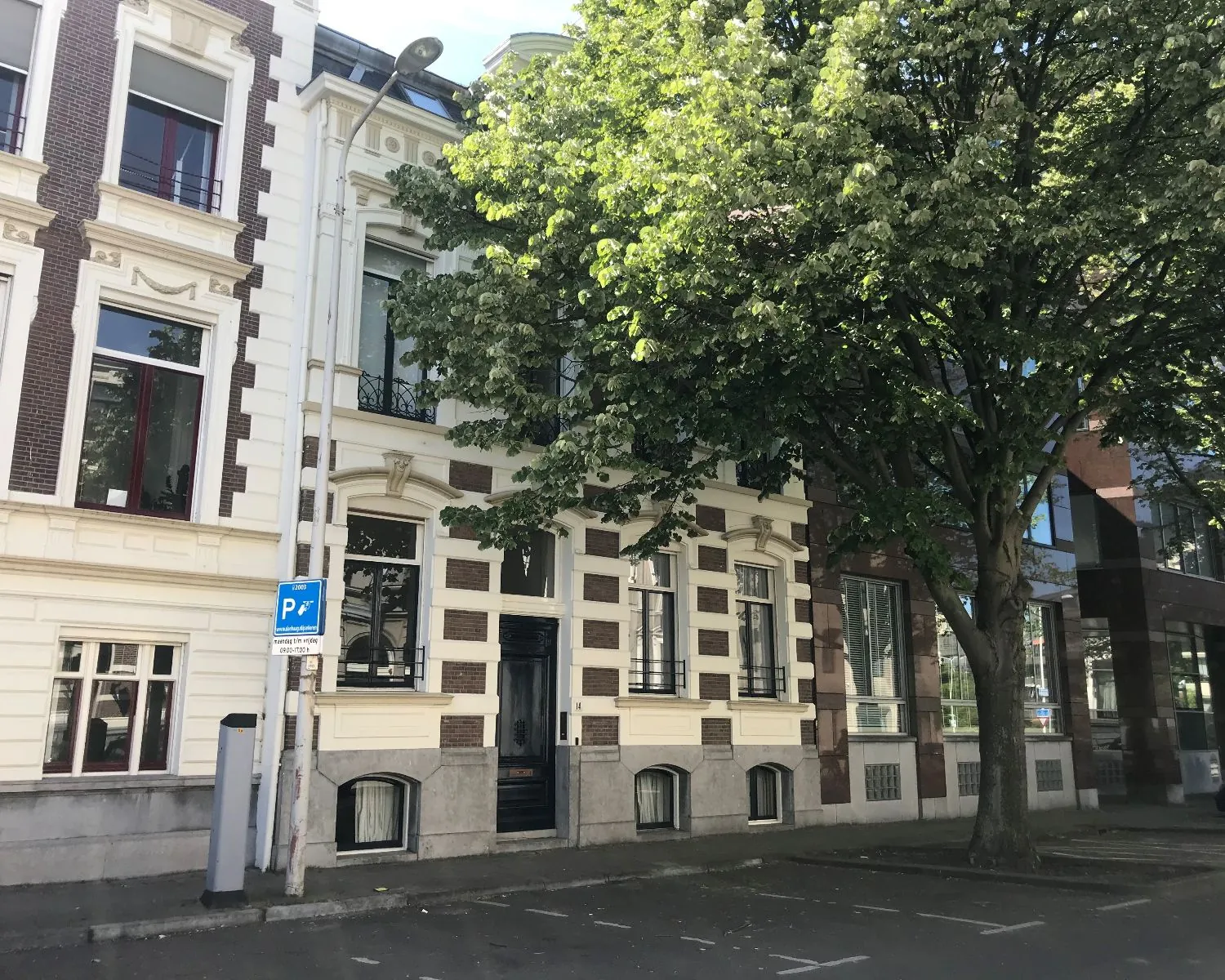 Voorgevel van een klassiek kantoorpand aan de Burgemeester van Karnebeeklaan 14 in Den Haag, gedeeltelijk beschaduwd door een grote boom.