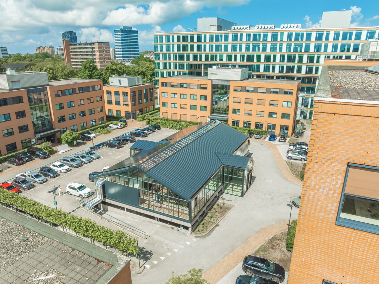 Luchtfoto van een modern kantoorgebouwcomplex met meerdere oranje en groene gebouwen en een glazen paviljoen in het midden.