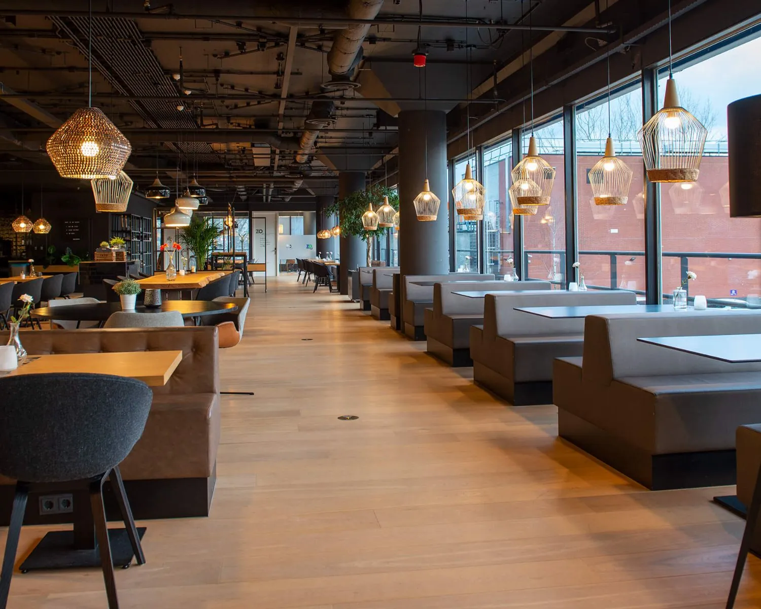 Modern restaurantinterieur in Groningen met houten vloer, grijze zitbanken en stijlvolle hanglampen.