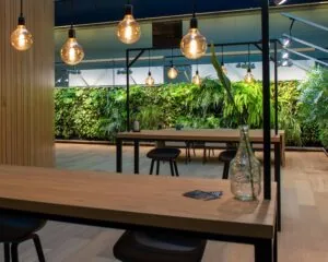 Modern interieur met houten tafels, hanglampen en een groene plantenwand in Groningen.