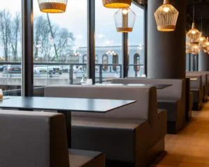 Moderne zithoeken in een stijlvol restaurant in Groningen met uitzicht op geparkeerde auto's en een boot buiten.
