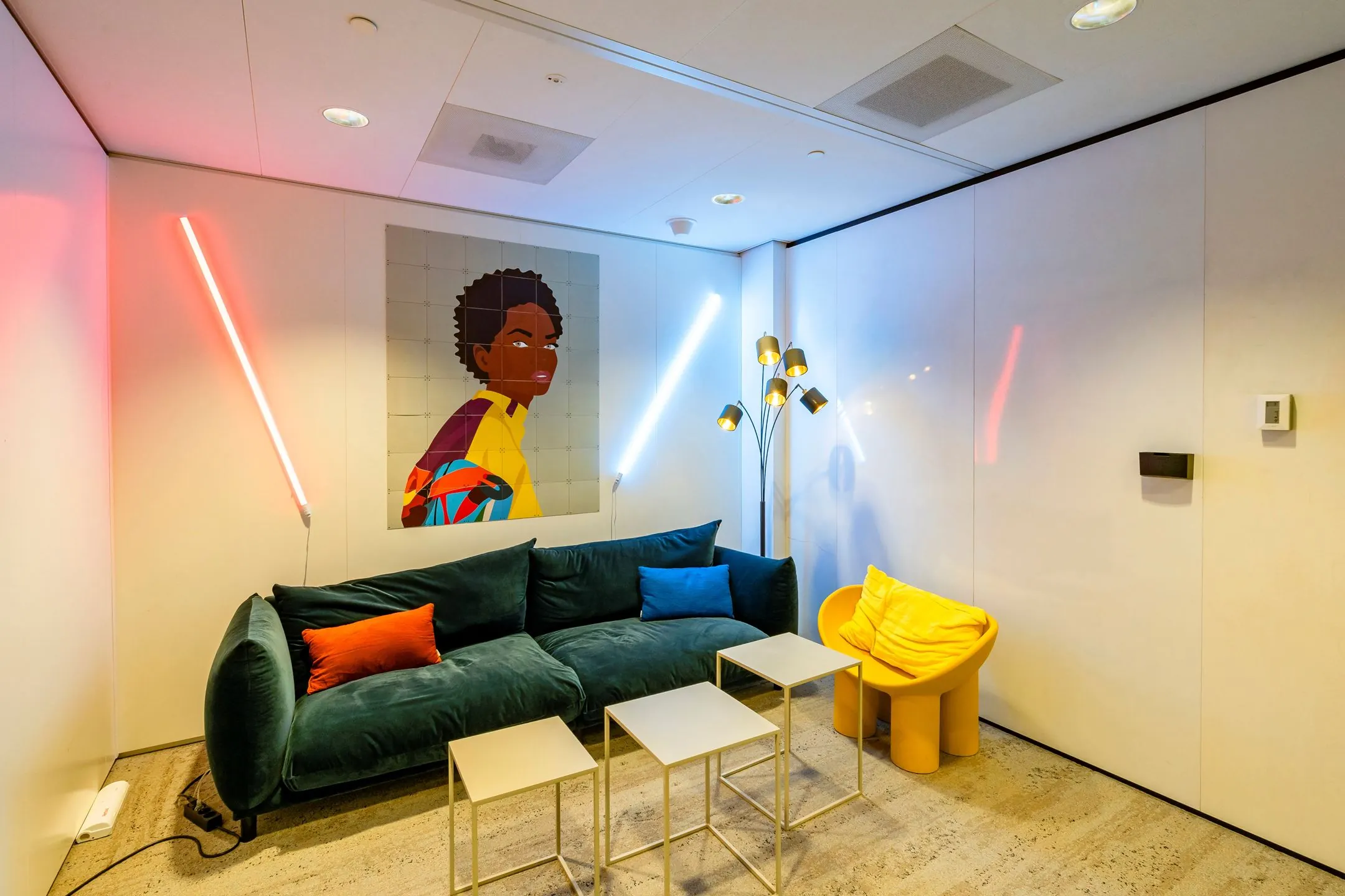 Modern ingerichte loungehoek op Gustav Mahlerlaan 1025 met kleurrijke meubels, neonverlichting en een opvallend portretschilderij aan de muur.