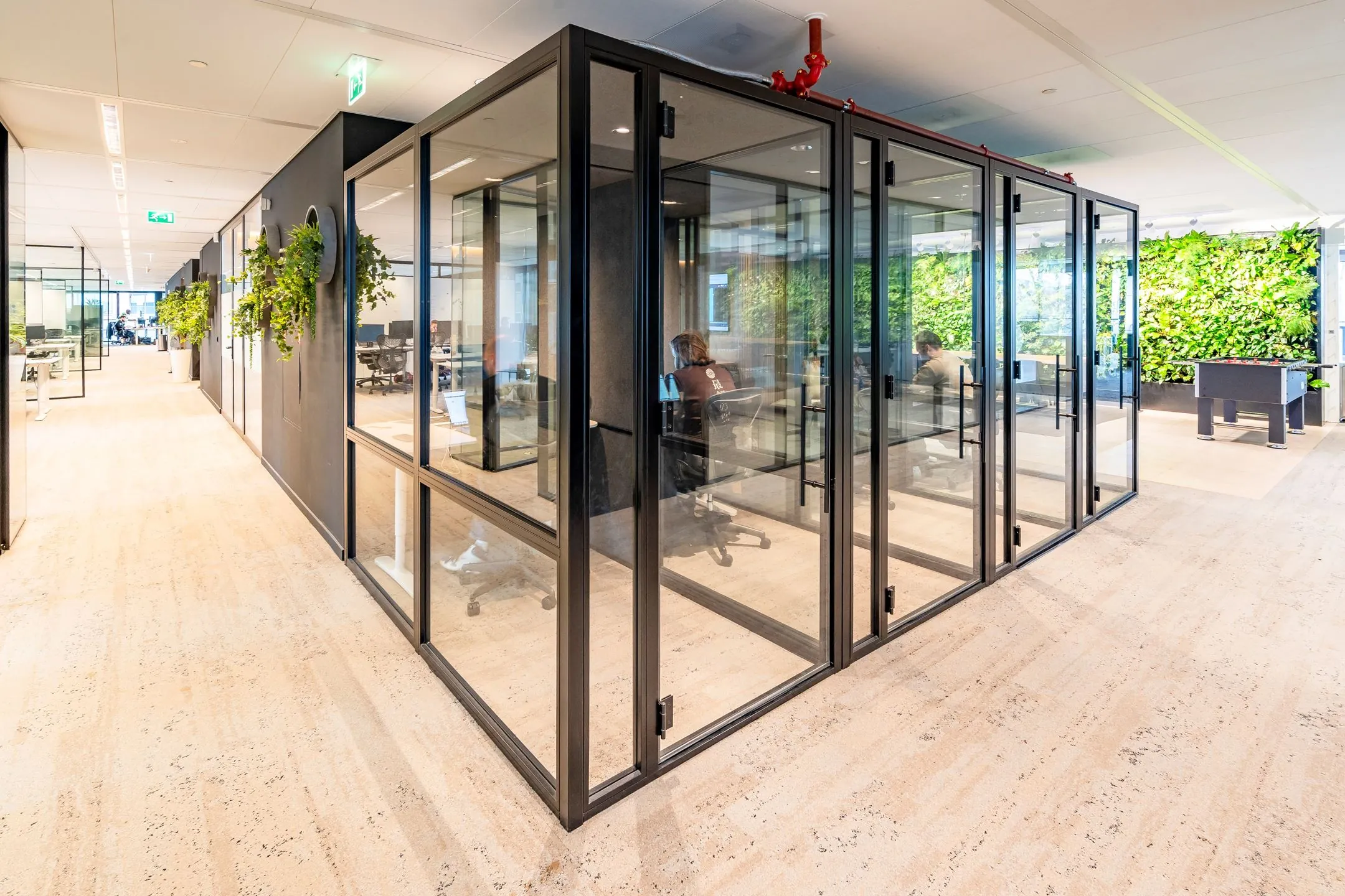 Moderne kantoorruimte aan de Gustav Mahlerlaan 1025 met glazen vergaderruimtes, groene wand en planten.