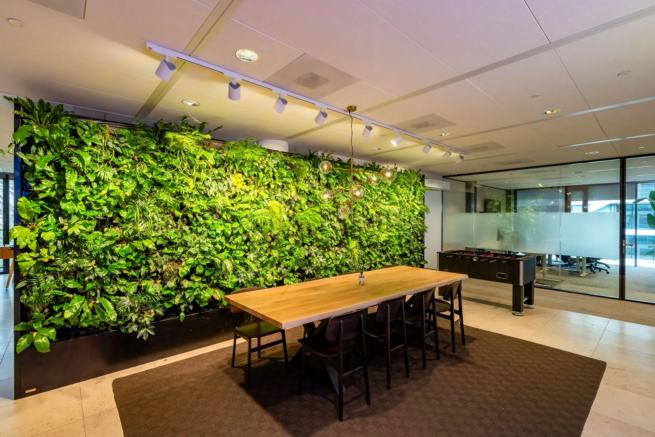 Vergaderruimte aan de Gustav Mahlerlaan met een grote houten tafel, groene plantenwand en glazen wanden.
