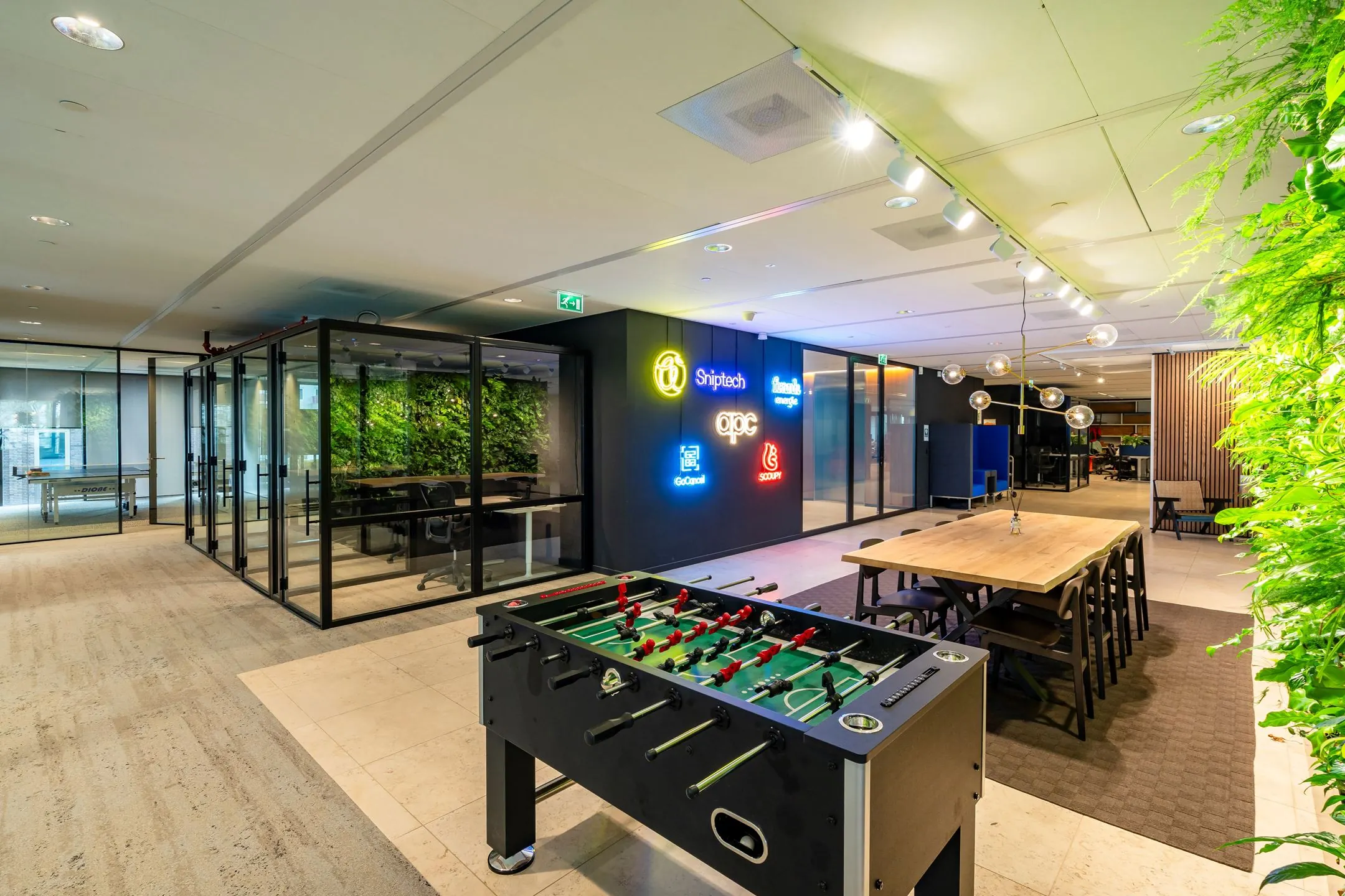 Moderne kantoorruimte aan de Gustav Mahlerlaan 1025 met een tafelvoetbaltafel, vergadertafel, glazen vergaderruimtes en verlichte bedrijfslogo’s aan de muur.