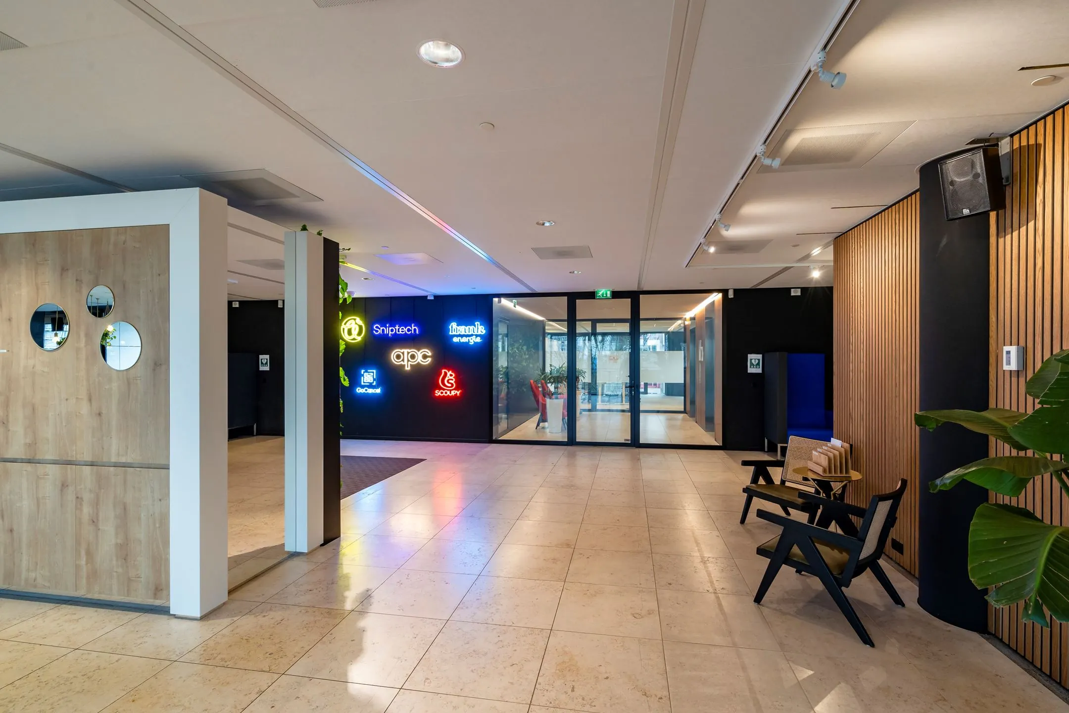 Moderne kantoorentree op Gustav Mahlerlaan 1025 met glazen deuren, houten accenten en verlichte bedrijfslogo’s aan de muur.