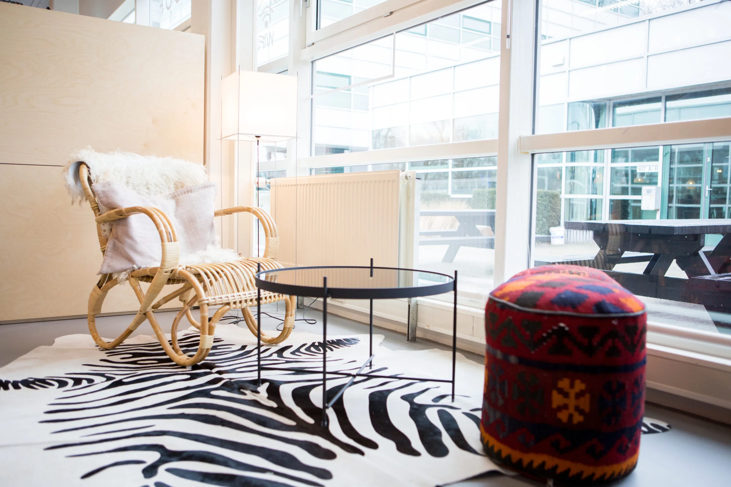 Zithoek met rotan stoel, zwart ronde tafel en kleurrijke poef in HNK Amsterdam Zuidoost.