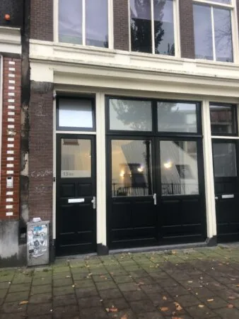 Vooraanzicht van het pand aan de Haarlemmer Houttuinen 15H met zwarte deuren en grote ramen.