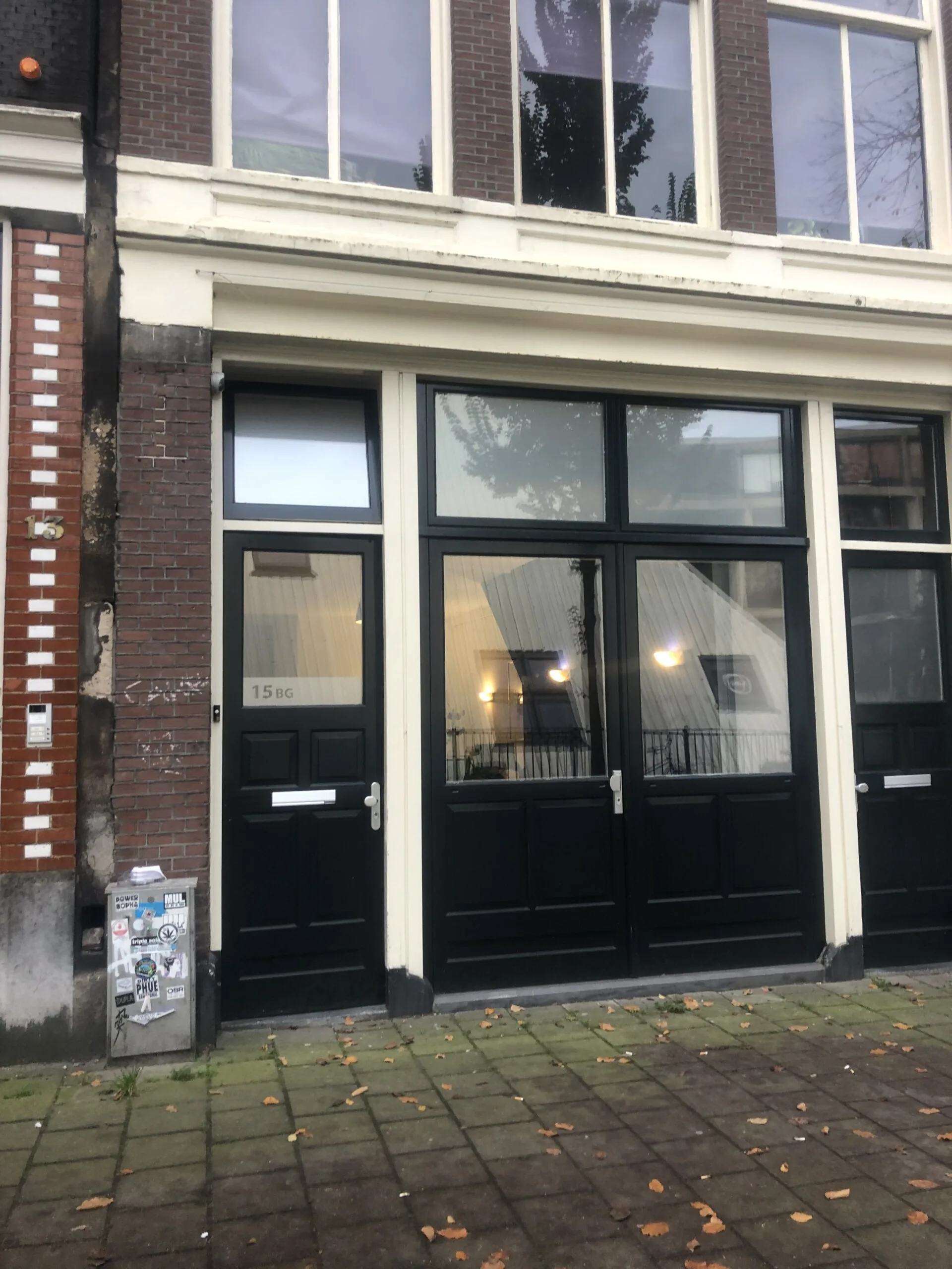 Vooraanzicht van het pand aan de Haarlemmer Houttuinen 15H met zwarte deuren en grote ramen.
