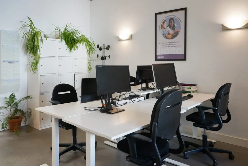 Moderne kantoorruimte aan de Haarlemmer Houttuinen 15H met bureaus, computers, stoelen, wandposter en kasten met hangplanten.