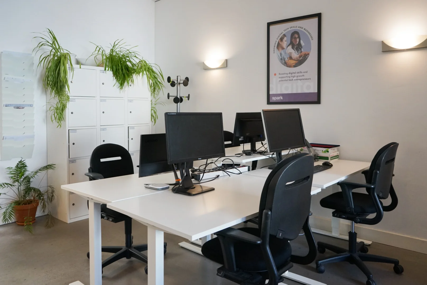 Moderne kantoorruimte aan de Haarlemmer Houttuinen 15H met bureaus, computers, stoelen, wandposter en kasten met hangplanten.
