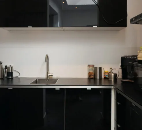 Moderne zwarte keuken met wit werkblad, ingebouwde spoelbak en koffieapparatuur op het aanrecht.