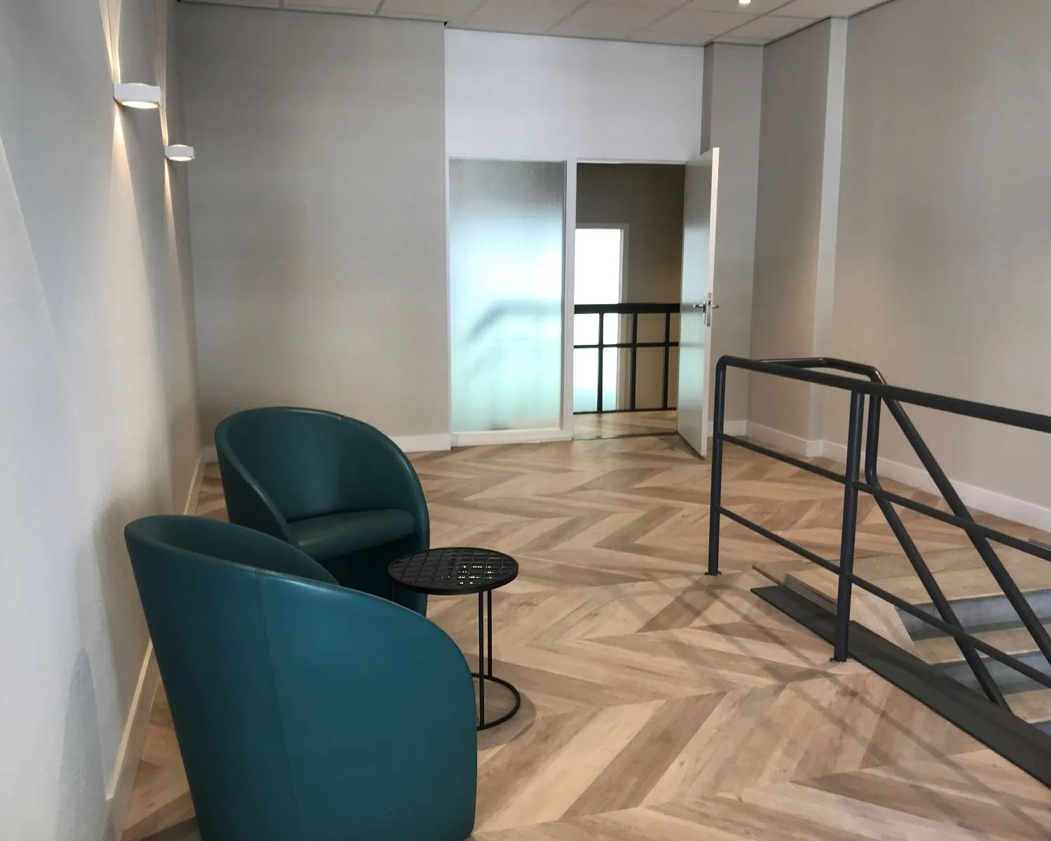Moderne hal in een kantoorpand aan de Burgemeester van Karnebeeklaan 14 in Den Haag met twee groene stoelen, een bijzettafel en een trap met zwart leuningwerk.