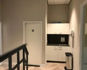 Kleine pantry met wastafel en keukenkastjes naast een toiletdeur in kantoorruimte aan de Burgemeester van Karnebeeklaan 14 in Den Haag.