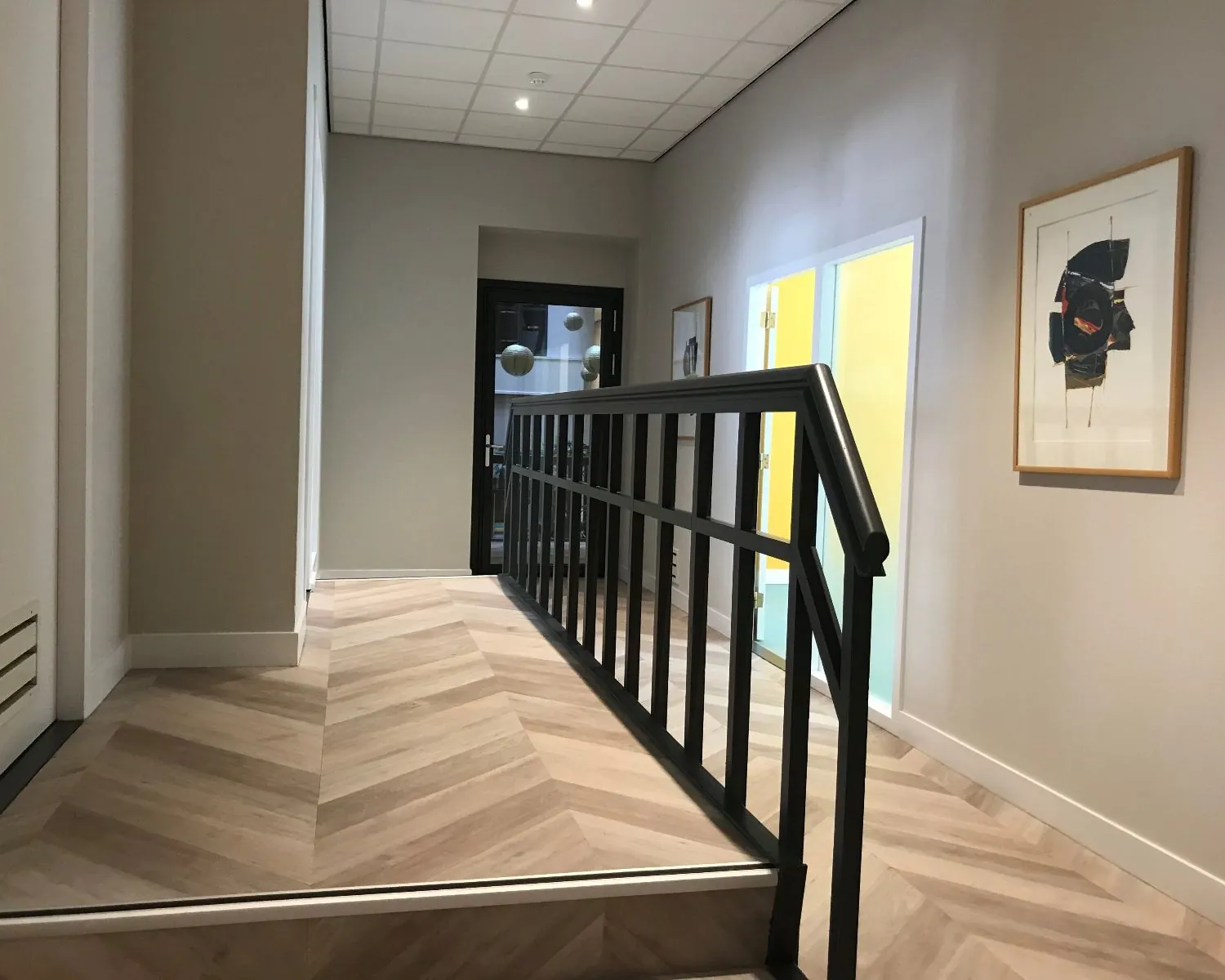 Moderne hal met visgraatvloer en zwarte leuning in kantoorpand aan de Burgemeester van Karnebeeklaan 14 in Den Haag.