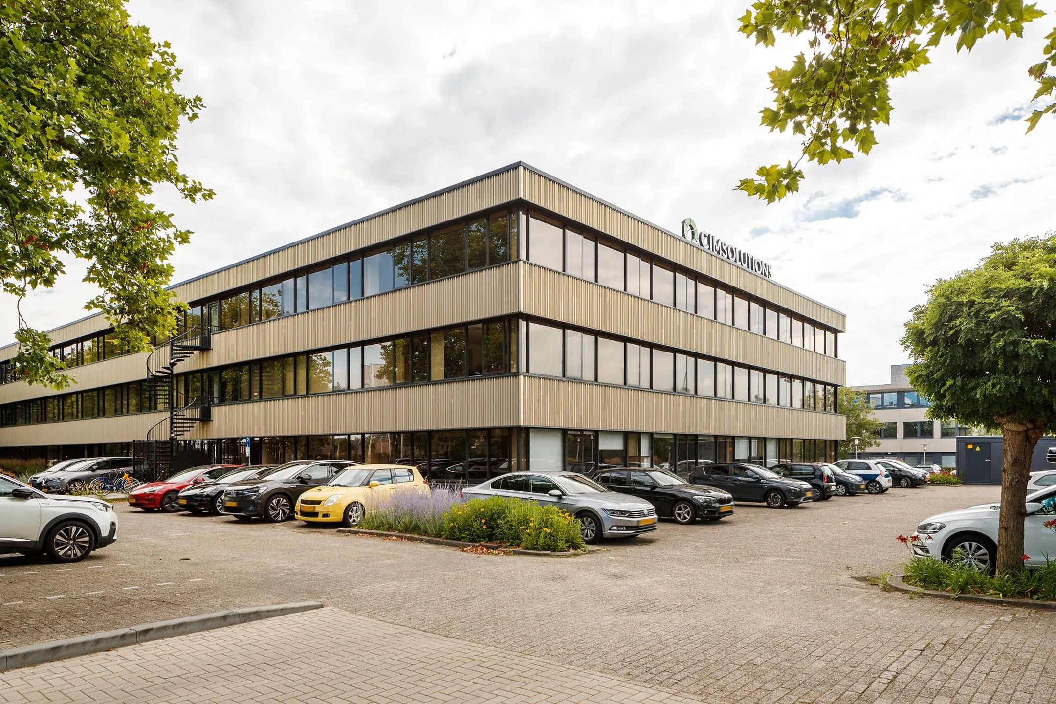 Kantoorgebouw aan de Havenweg 24 met parkeerplaats vol auto's op de voorgrond.