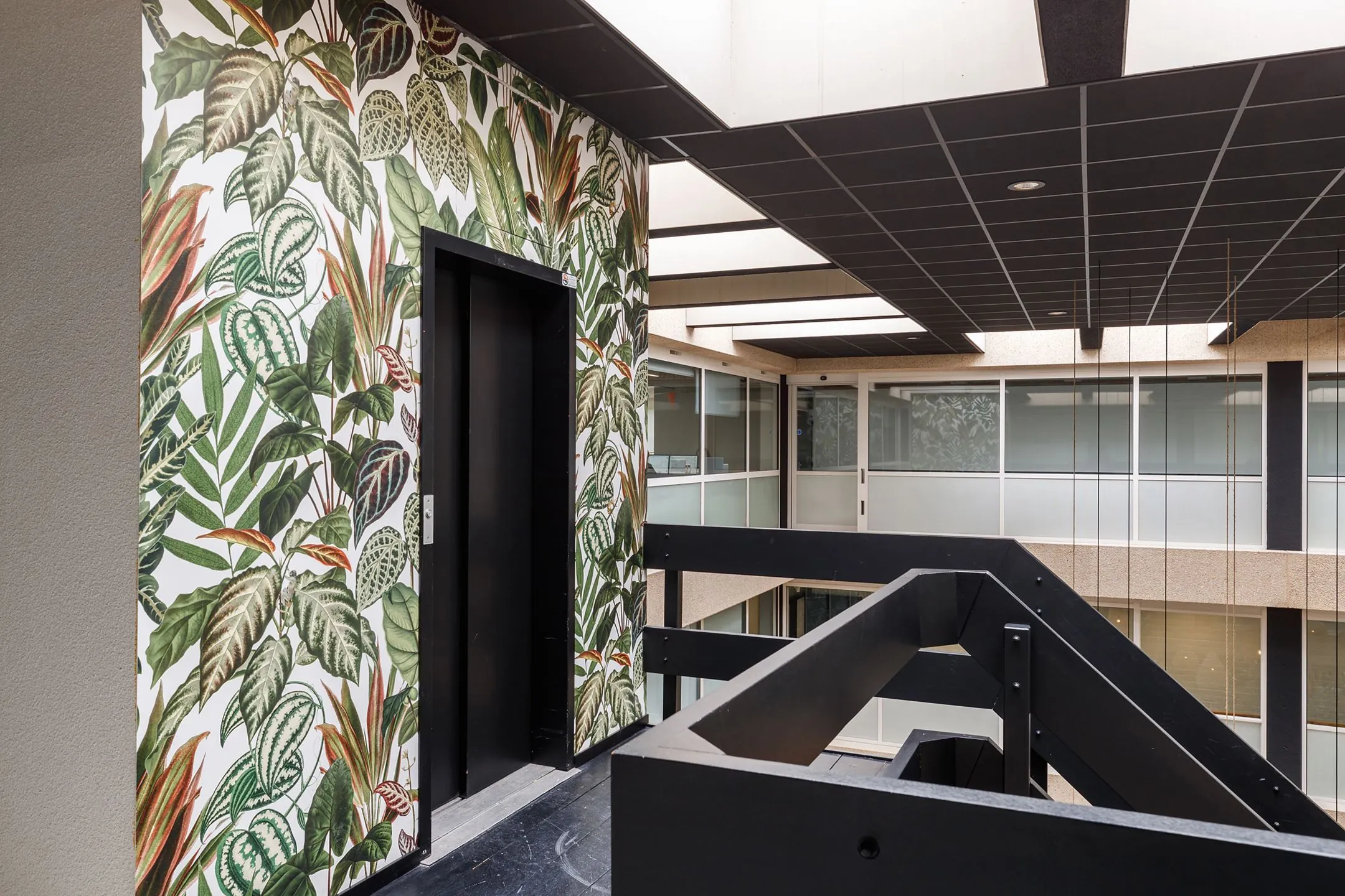 Binnenruimte van een modern kantoor aan de Havenweg 24 met een liftomkleding voorzien van tropisch plantenbehang.