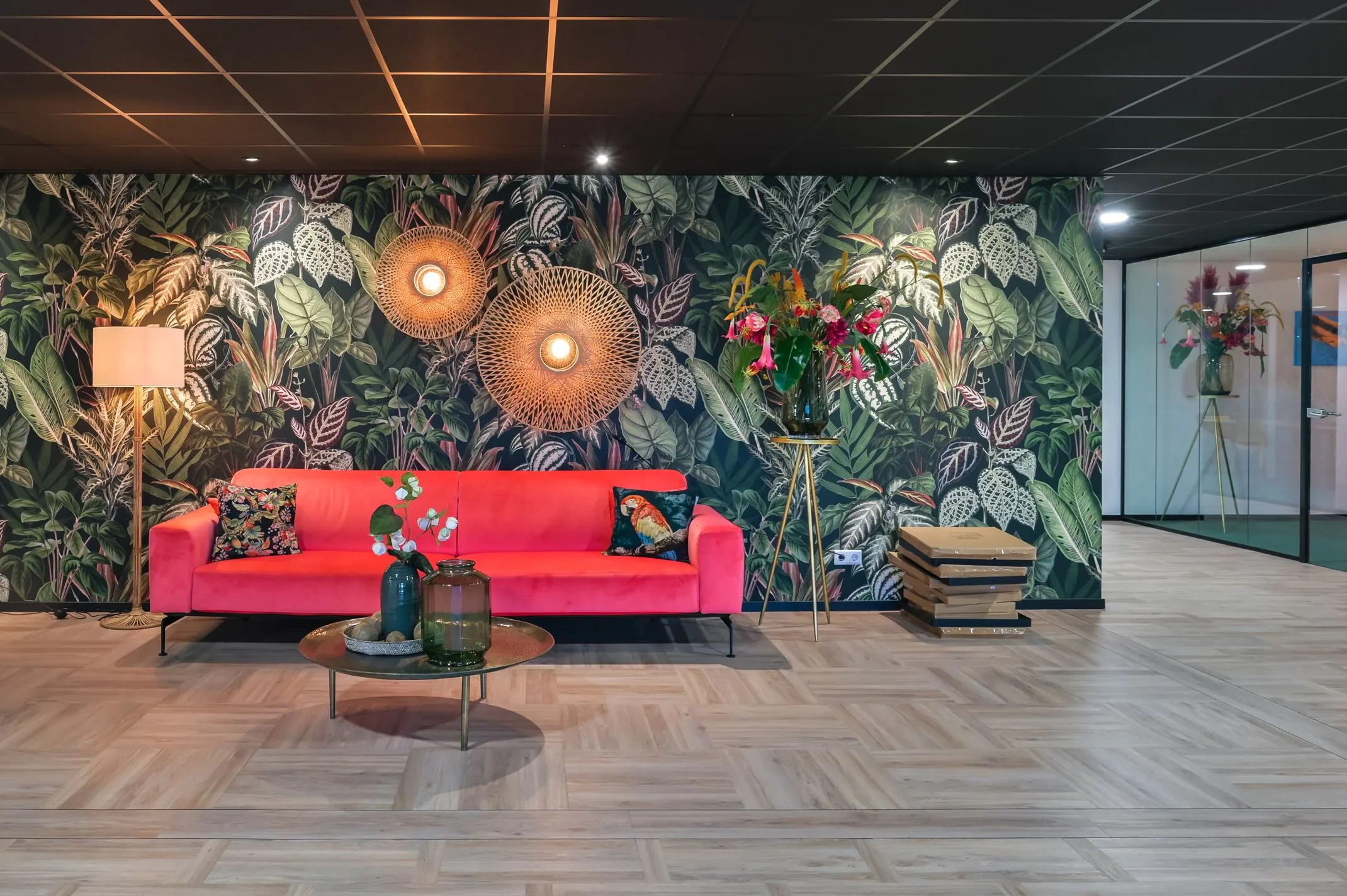 Moderne wachtruimte aan Havenweg 24 met een felroze bank, tropisch behang, grote bloemenvaas en sfeerverlichting.