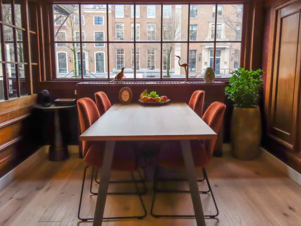 Eettafel met roodfluwelen stoelen in een sfeervolle kamer aan Herengracht 449, met uitzicht op Amsterdamse grachtenpanden.