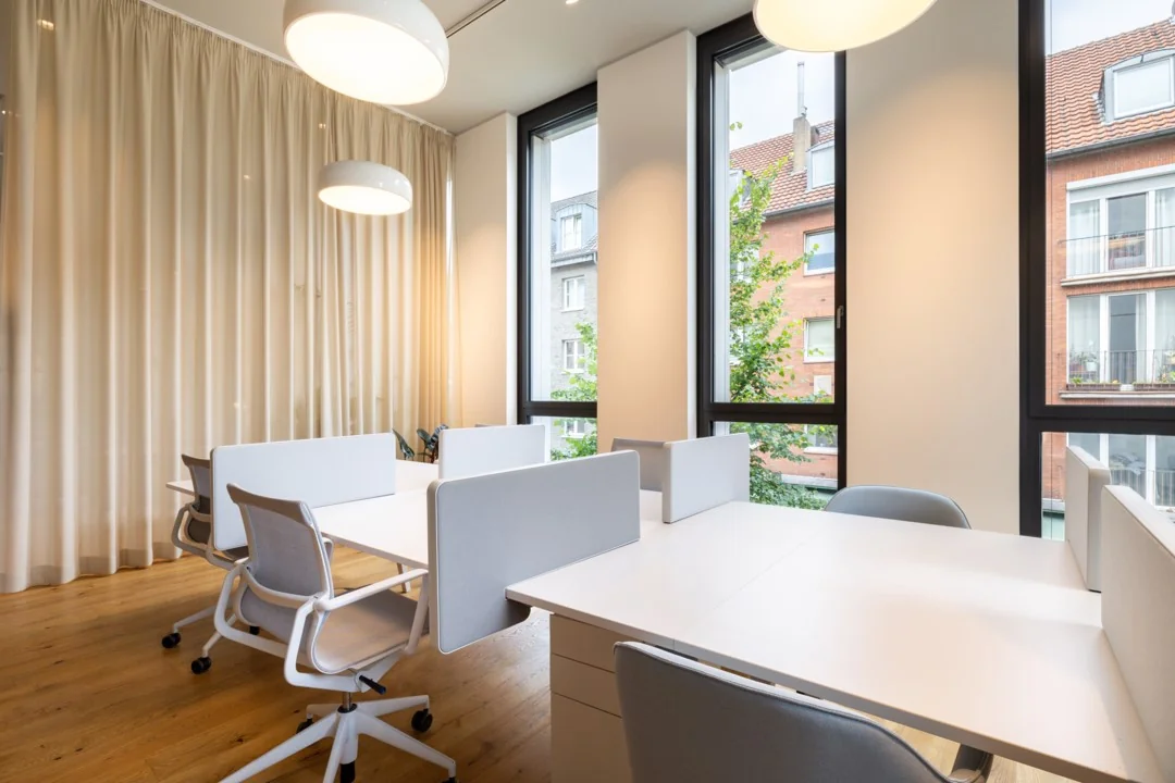 Moderne kantoorruimte aan de Hoogstraat 1001 met witte bureaus, ergonomische stoelen en grote ramen met uitzicht op omliggende gebouwen.
