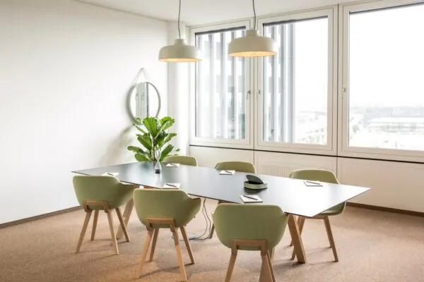 Moderne vergaderruimte met zes groene stoelen, een zwarte tafel, grote ramen en een plant bij Hoogstraat 1001.