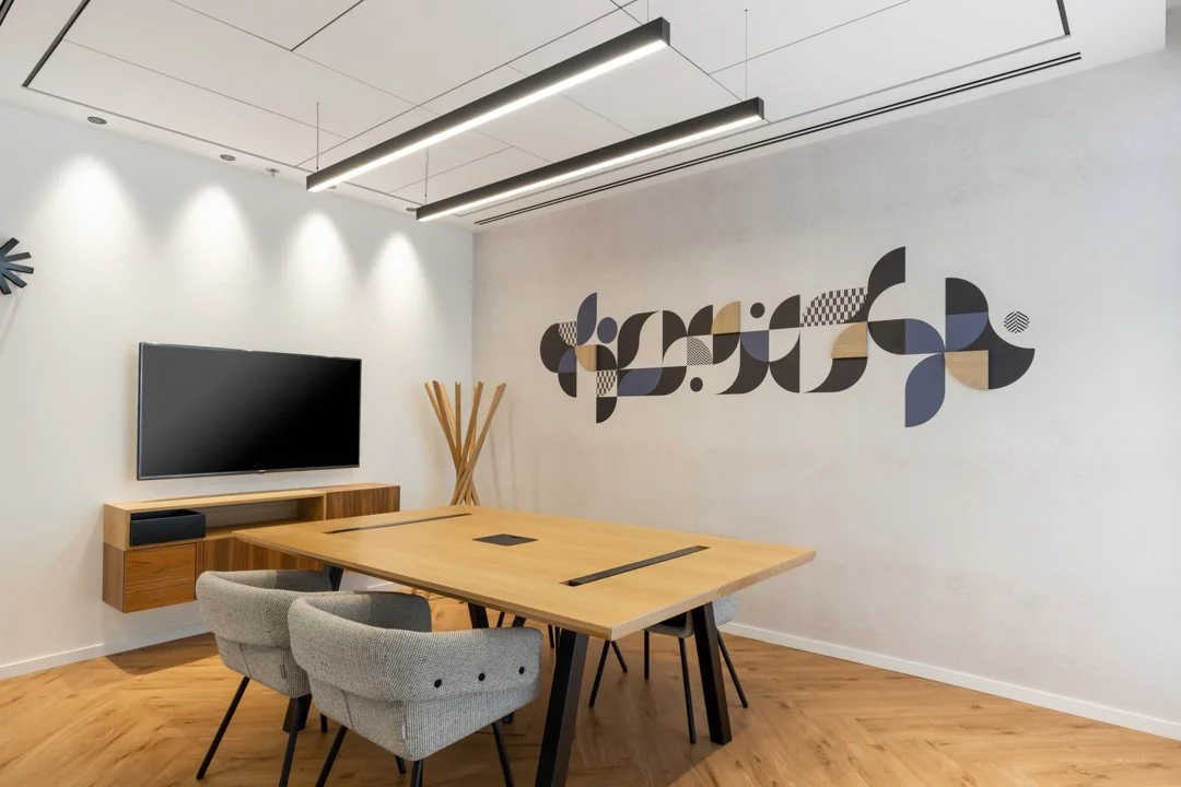 Moderne vergaderruimte met houten tafel, grijze stoelen, muurkunst en een flatscreen aan de muur.
