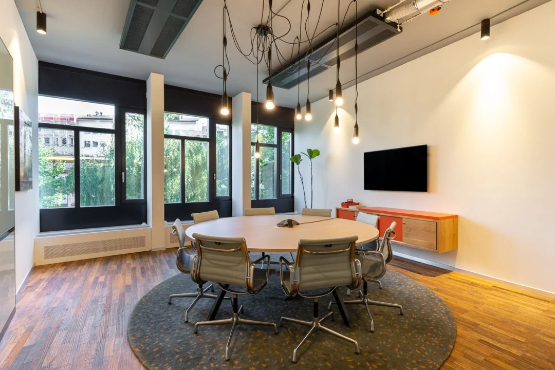 Moderne vergaderruimte aan de Hoogstraat 1001 met ronde tafel, designstoelen, hanglampen en grote ramen met uitzicht op groen.