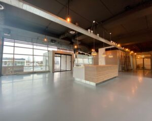 Moderne, lichte bedrijfsruimte met houten balie, grote ramen en industriële verlichting.