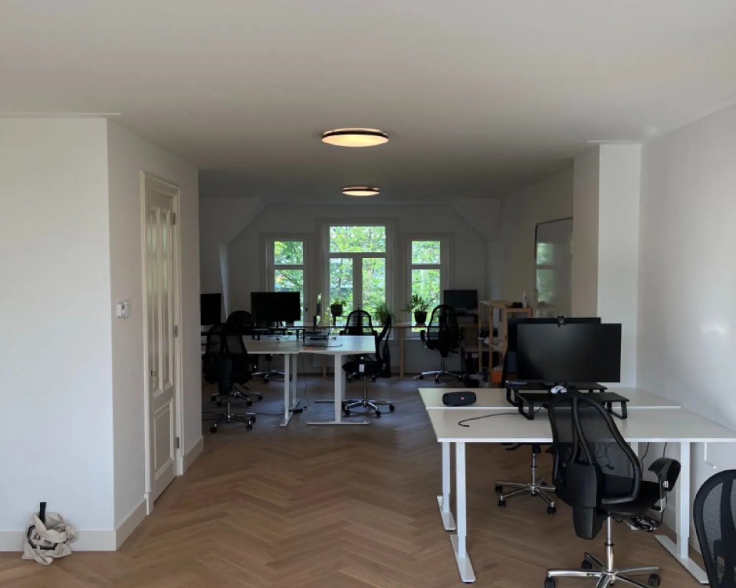 Moderne, lichte kantoorruimte met meerdere bureaus, computerschermen en ergonomische stoelen.