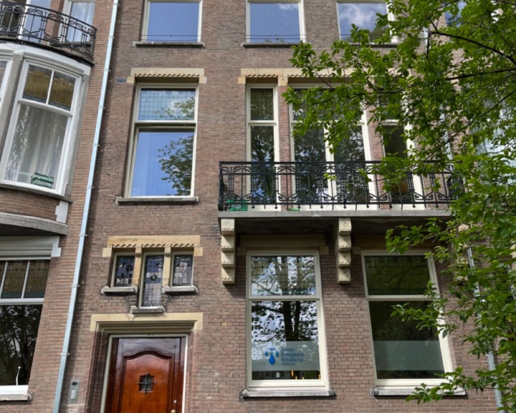 Voorgevel van een traditioneel herenhuis met grote ramen, een balkon en een boom op de voorgrond.