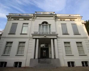 Vooraanzicht van een groot wit herenhuis met klassieke architectuur en zuilen bij de ingang.