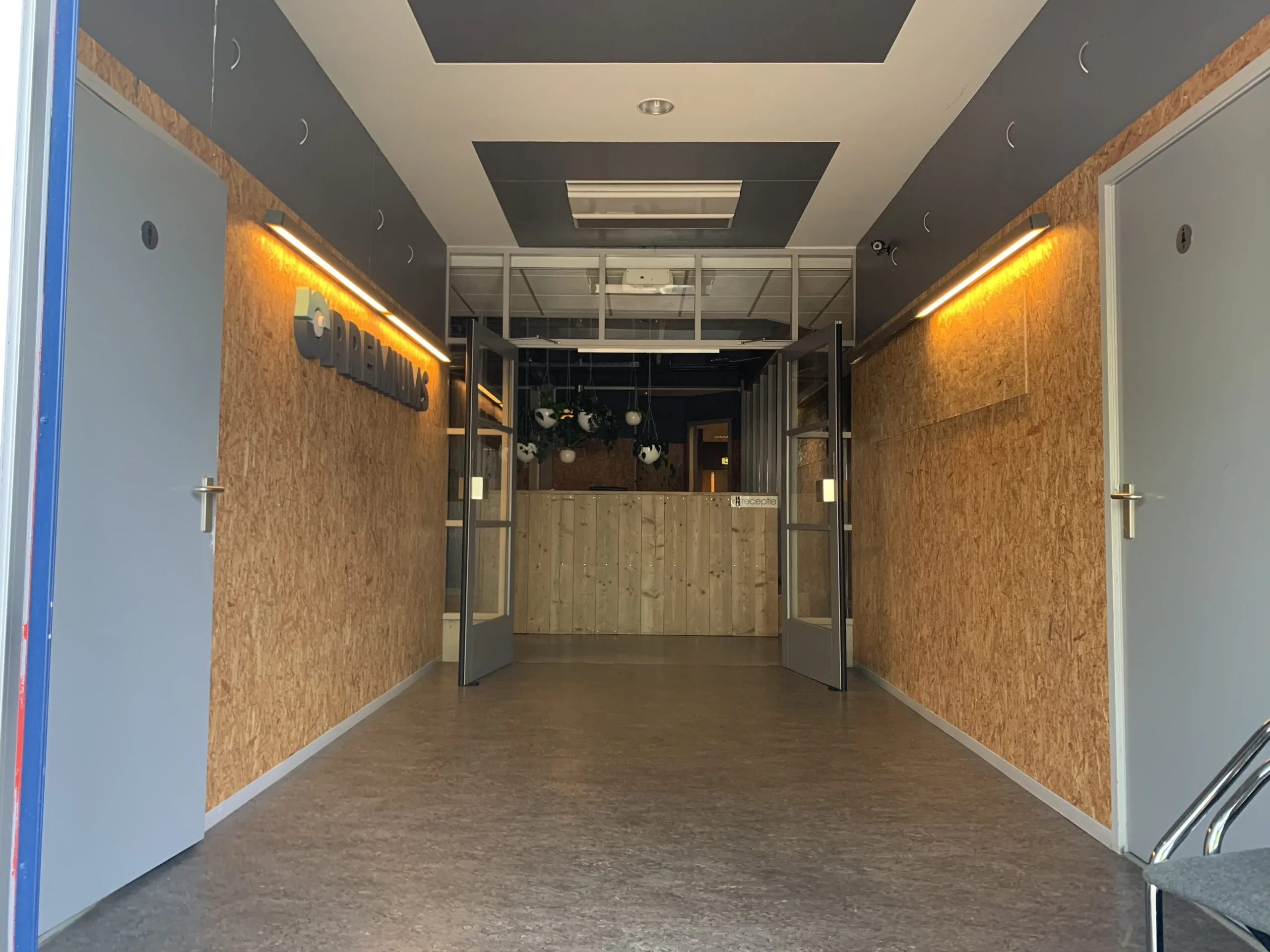 Hal met houten wandpanelen, grijze deuren en een bord met de tekst "CREDENHILL" bij de ingang van een gebouw.