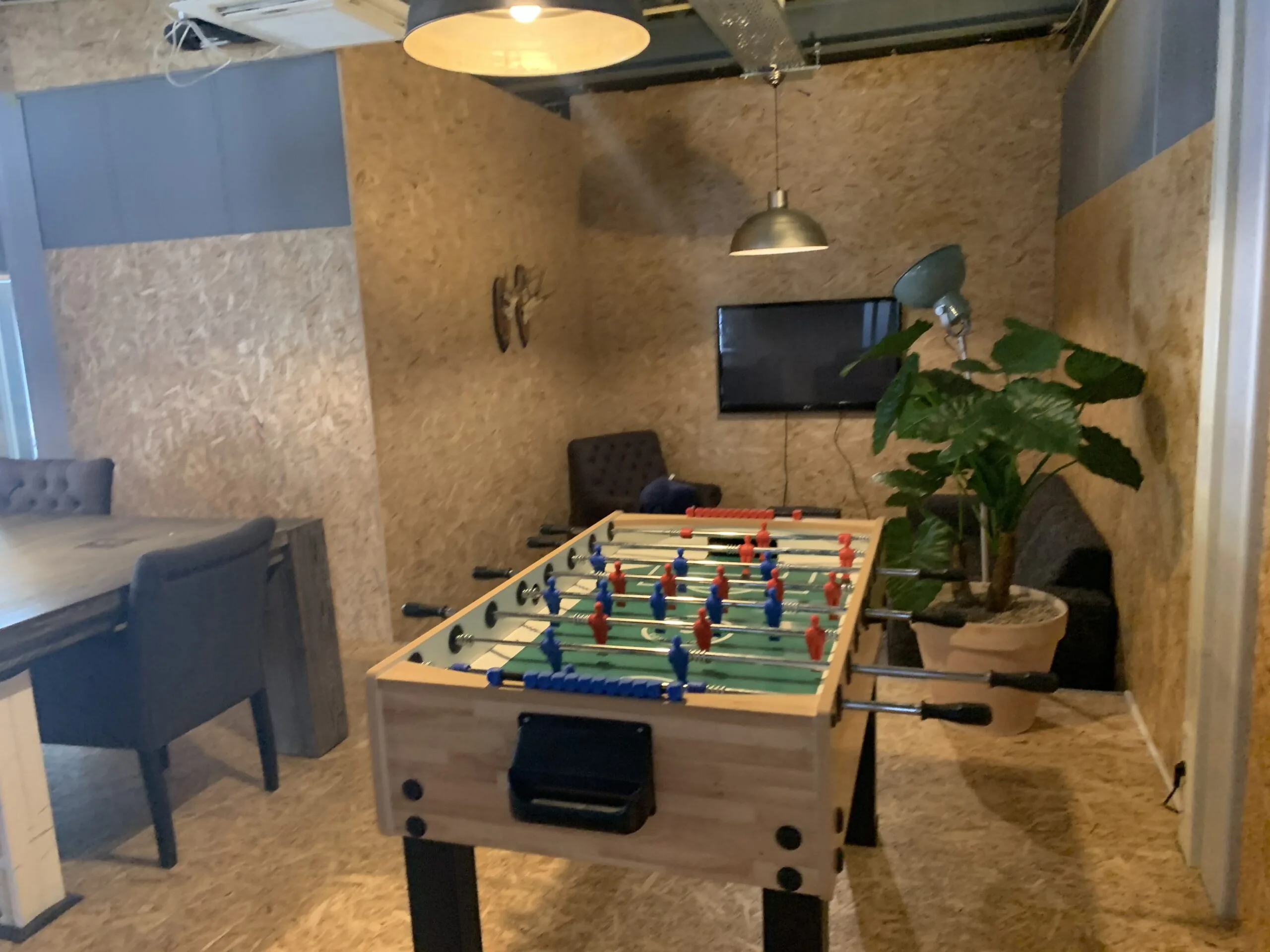 Kantoorlounge met een tafelvoetbaltafel, zithoek, televisiescherm en grote kamerplant.