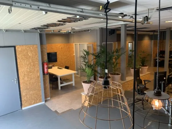 Moderne kantoorruimte met houten wanden, bureaus, groene planten en industriële verlichting.