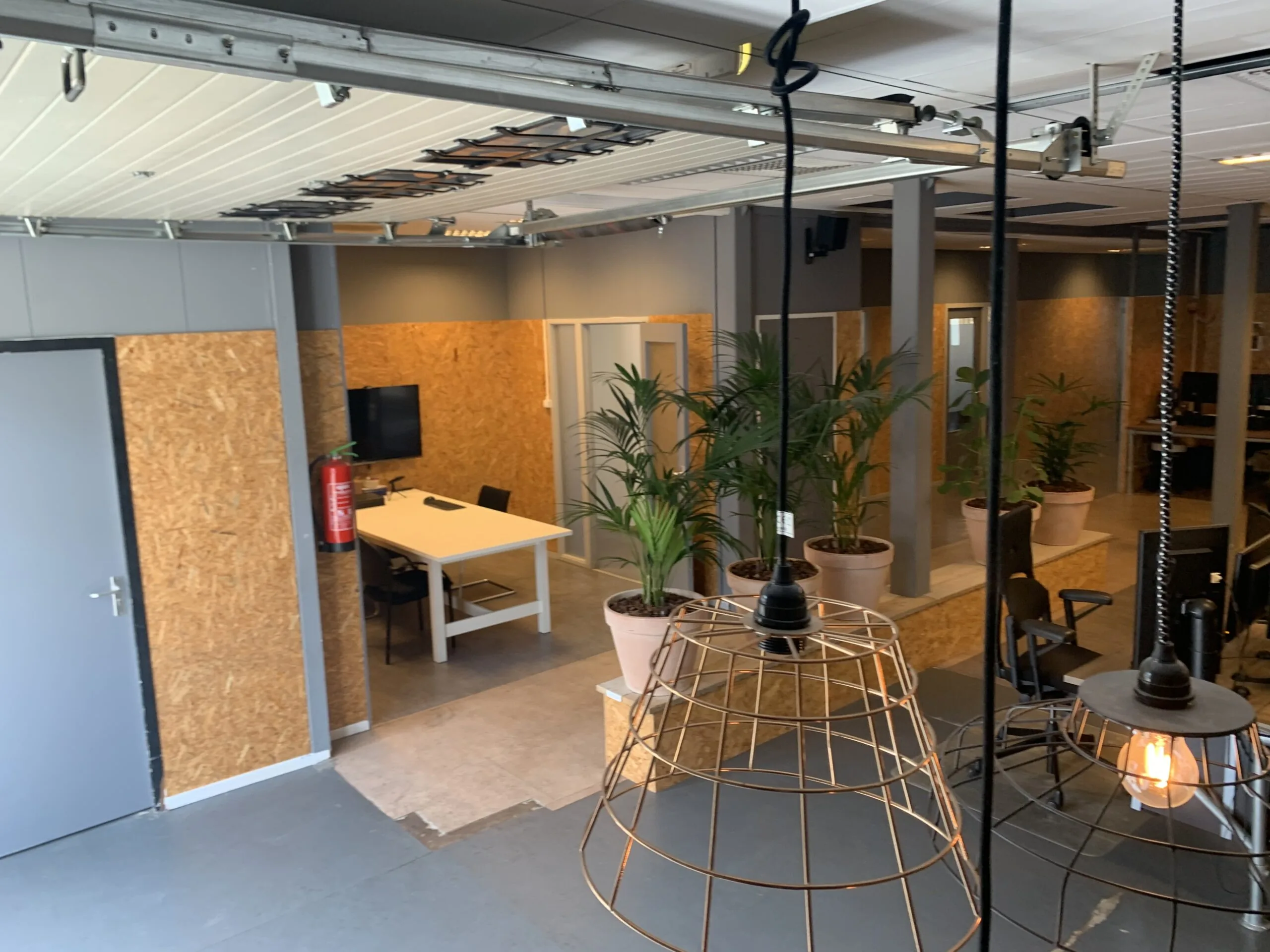 Moderne kantoorruimte met houten wanden, bureaus, groene planten en industriële verlichting.