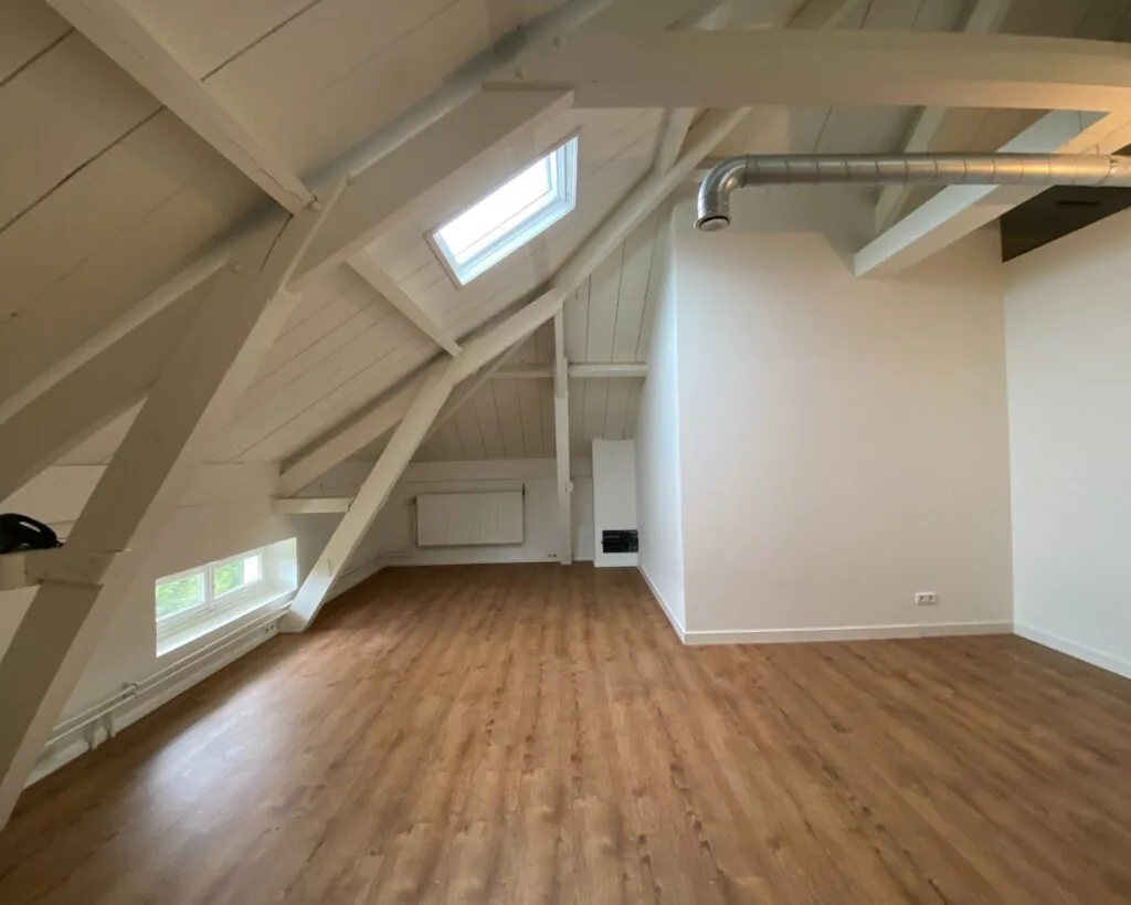 Zolderkamer met schuin houten dak, dakraam en laminaatvloer.